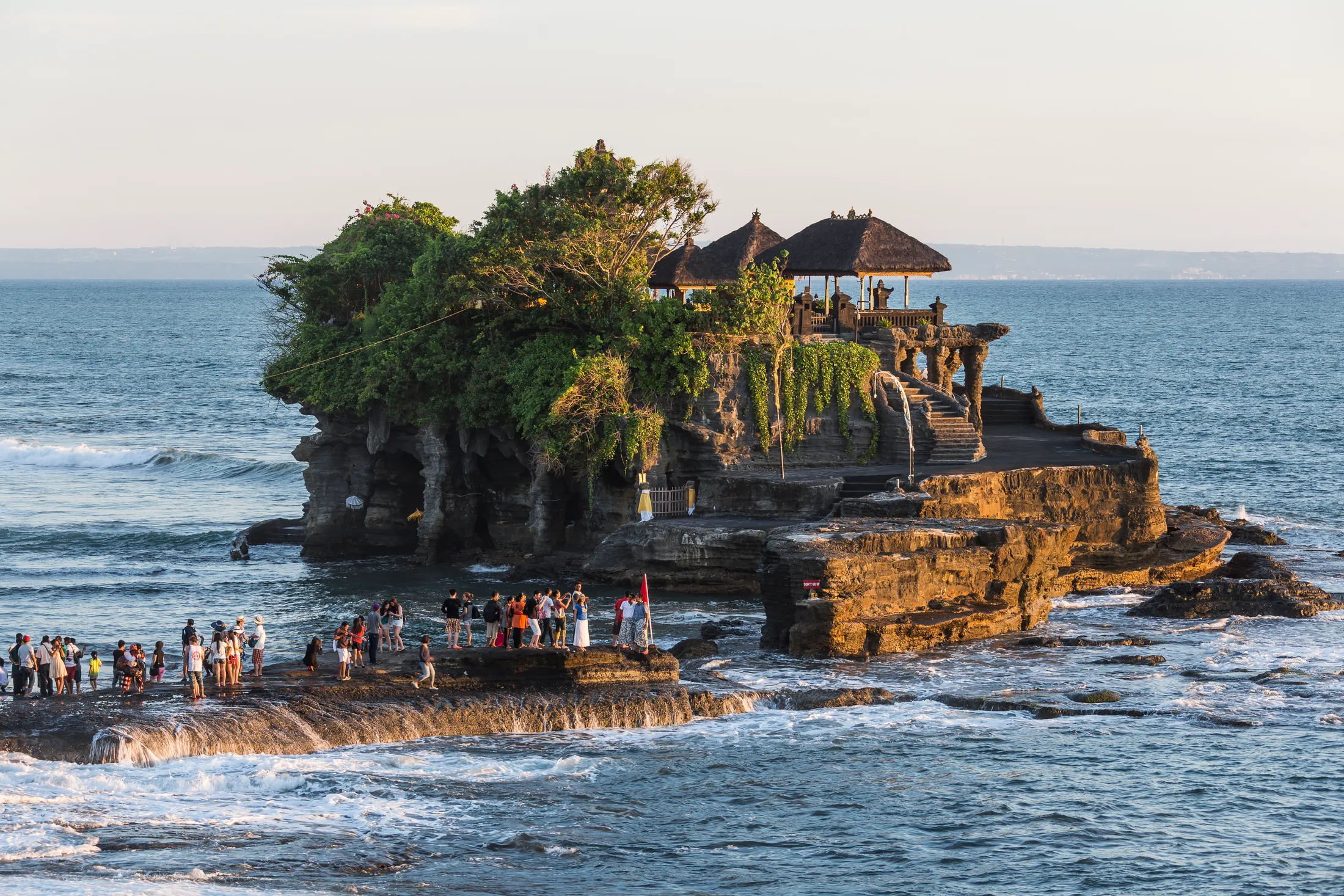 Pura Tanah Lot on its rock offshore in late light, visitors on the causeway below it