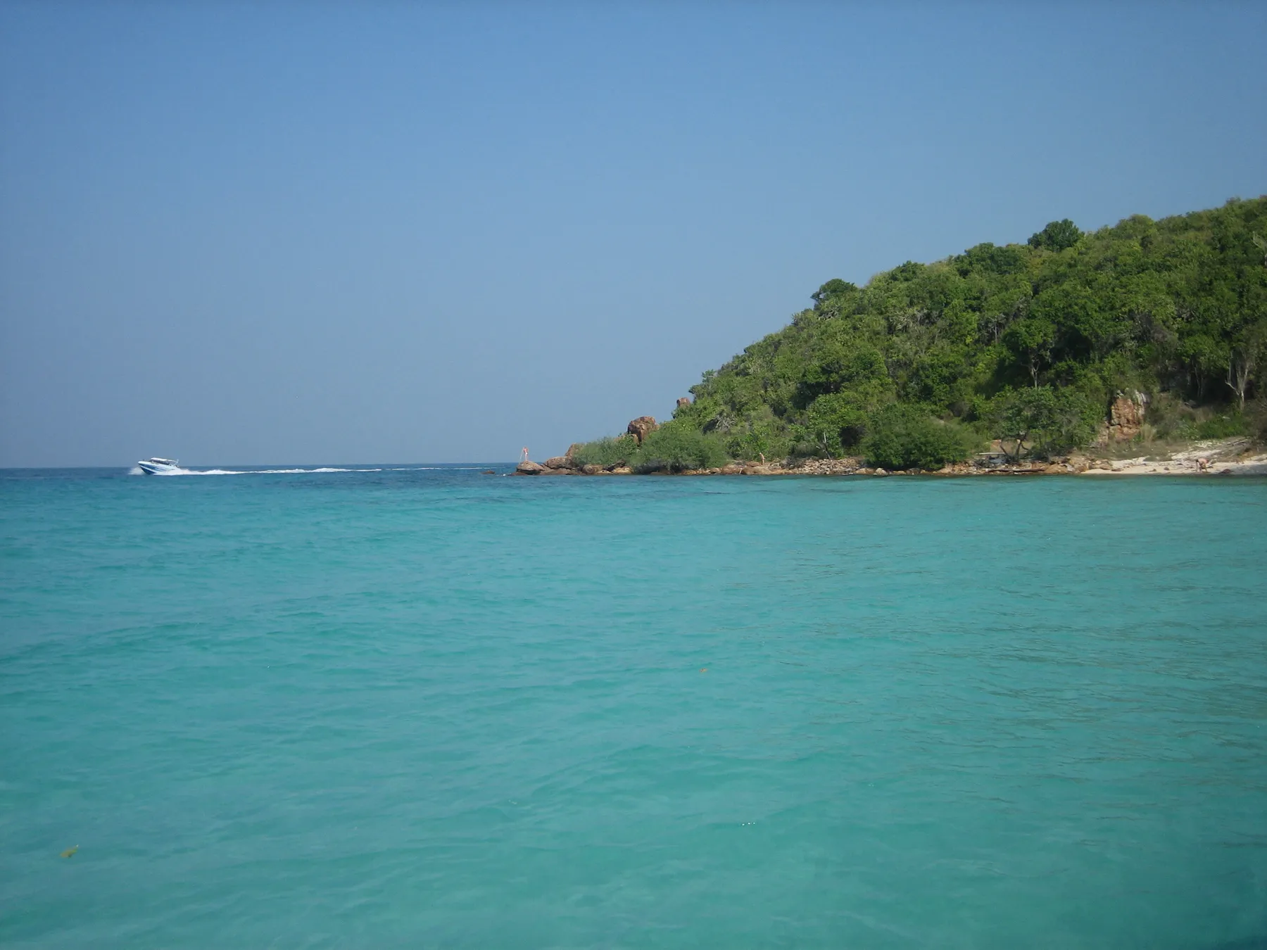 The green headland and turquoise shallows of Koh Larn off Pattaya, a speedboat running past