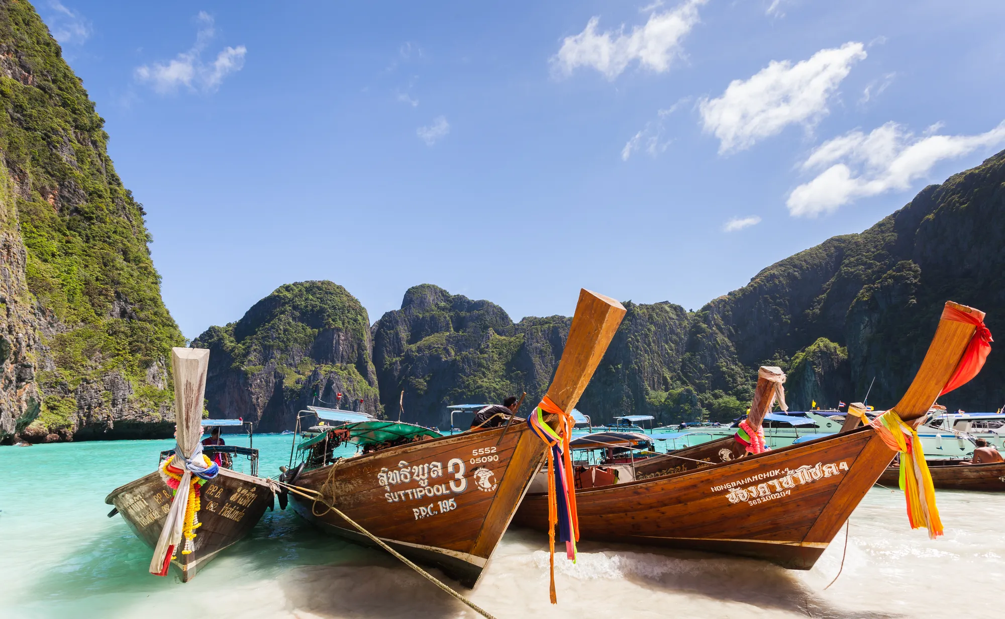 Longtail boats drawn up on the sand at Maya Bay, Ko Phi Phi Ley, limestone cliffs behind